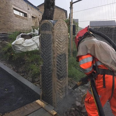 Blaster in orange overalls and a blasting helmet removing grime from brick