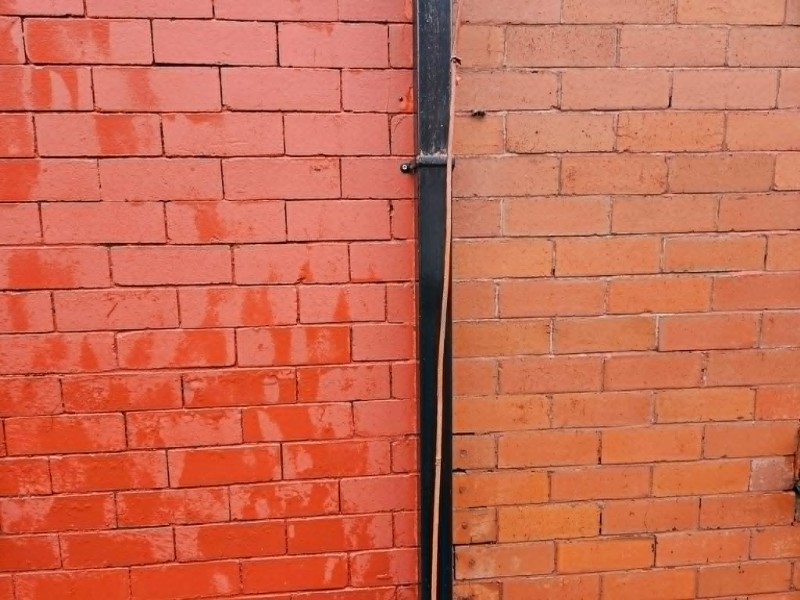 man in wetsuit on a ladder pressure cleaning white paint off brickwork to house